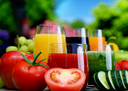 A table topped with glasses of juice and vegetables.