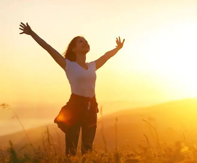 A woman standing in the sun with her arms outstretched.