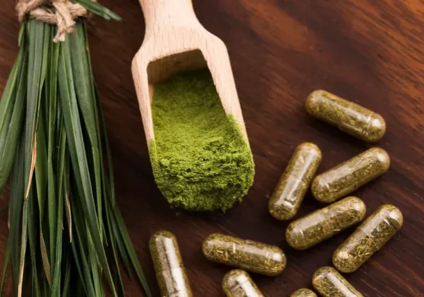 A wooden spoon with green powder on it next to some pills.